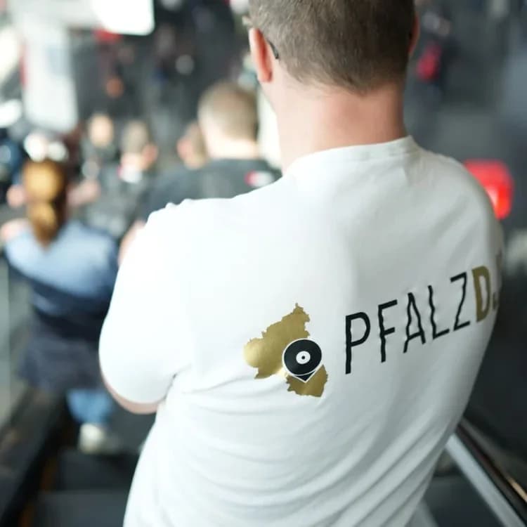 Weißes T-Shirt aus eigener Werkstatt-Produktion mit goldenem Pfalz-DJs-Wortmark, getragen auf einer Messe
